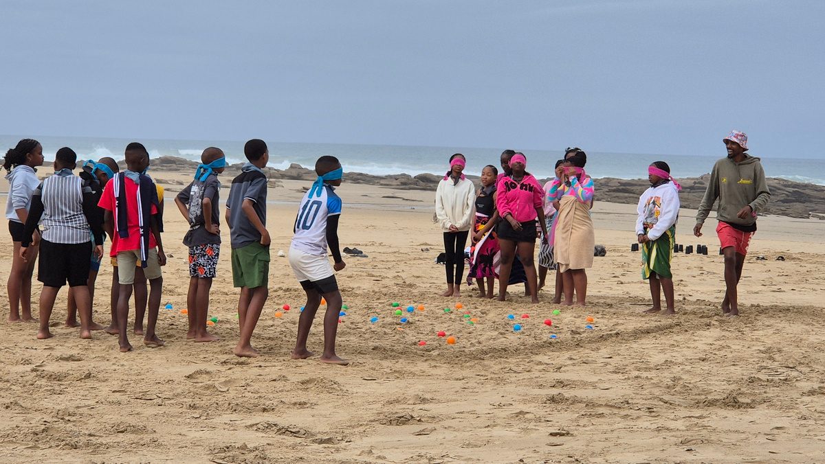 Learners playing a blindfolded team game on the sand